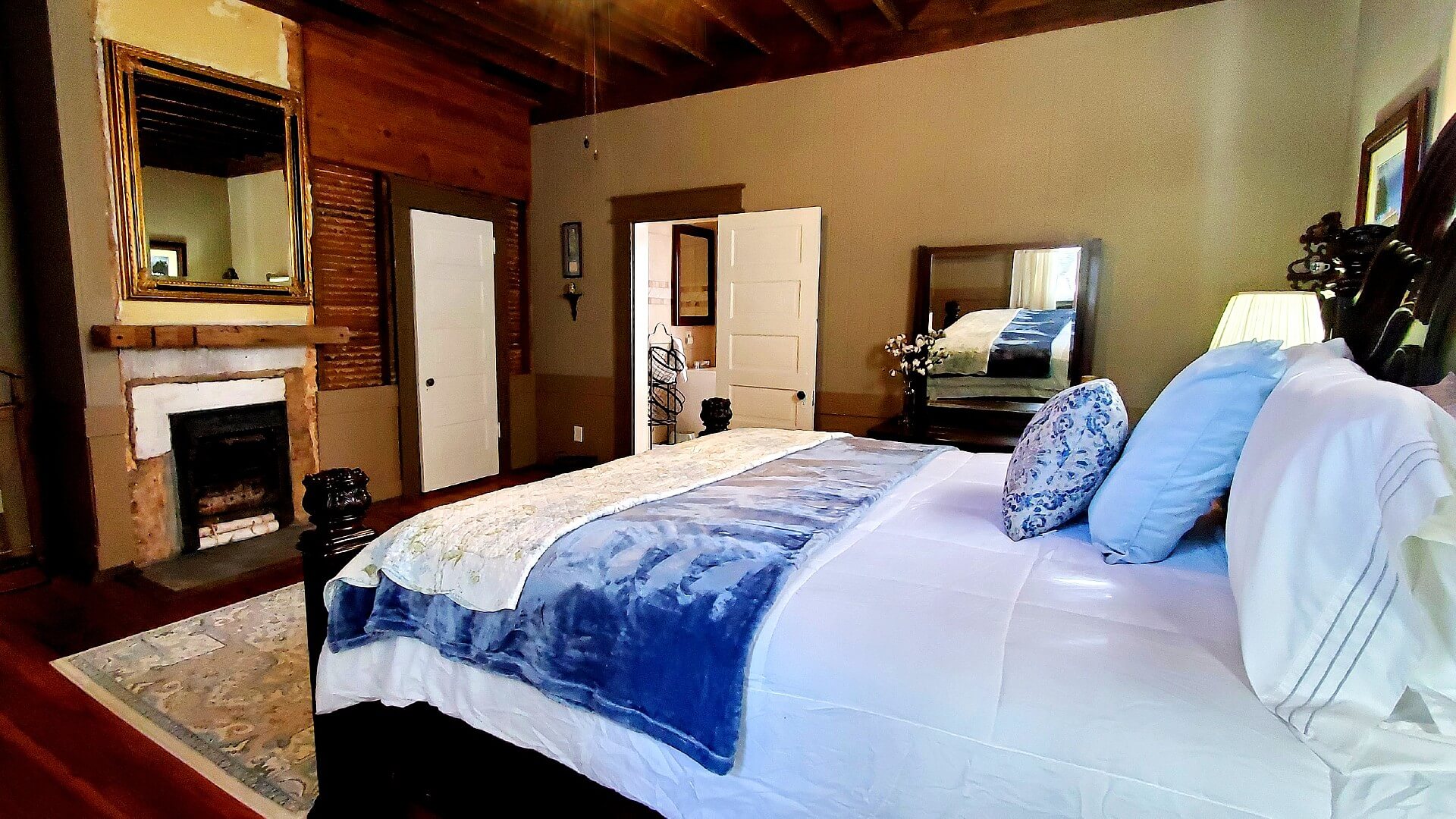 Spacious bedroom with queen bed in white and blue linens, fireplace and doorway into a bathroom